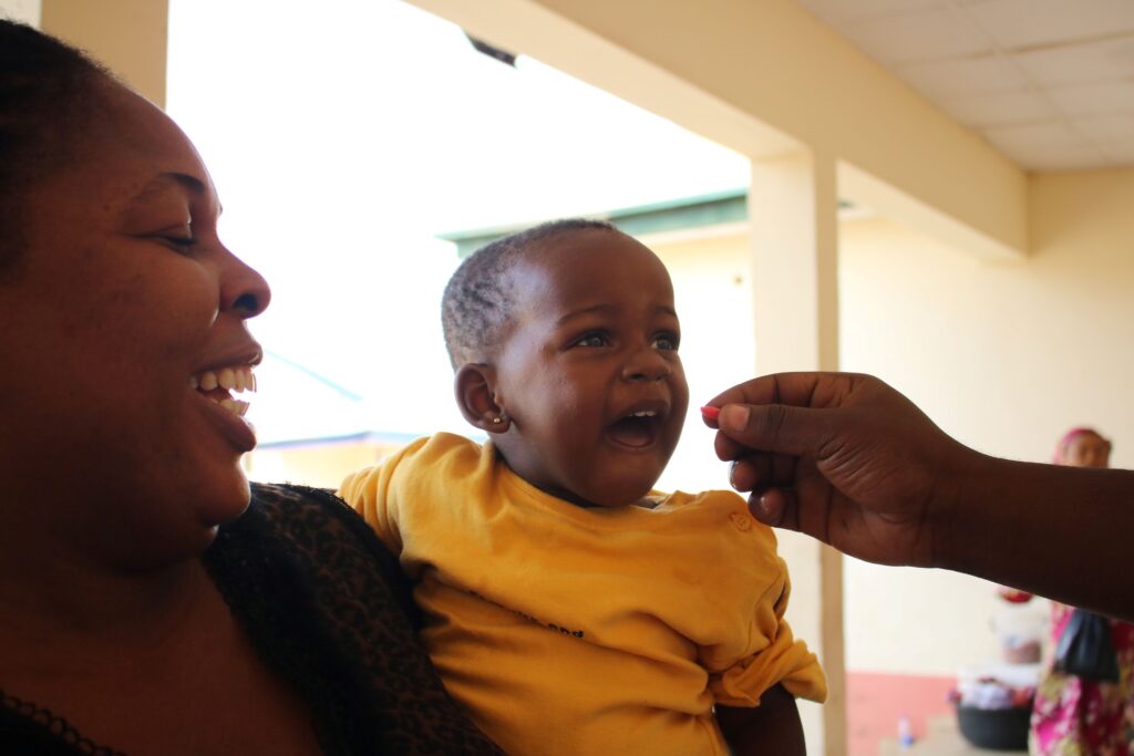 Young child receiving vitamin A supplementation while being held by mother