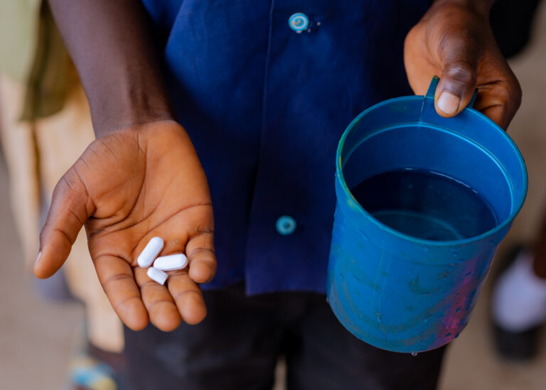 Hand holding pills and blue cup of water