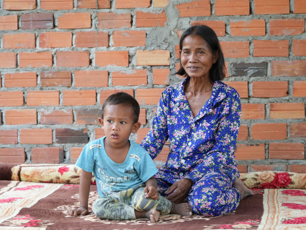 Grandmother and grandson sitting together on the ground in front of their home.
