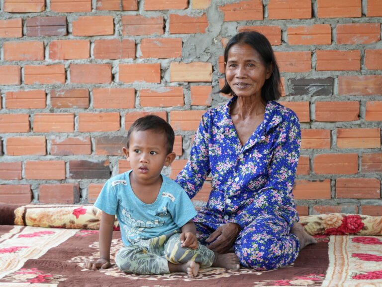 Grandmother and grandson sitting together on the ground in front of their home.