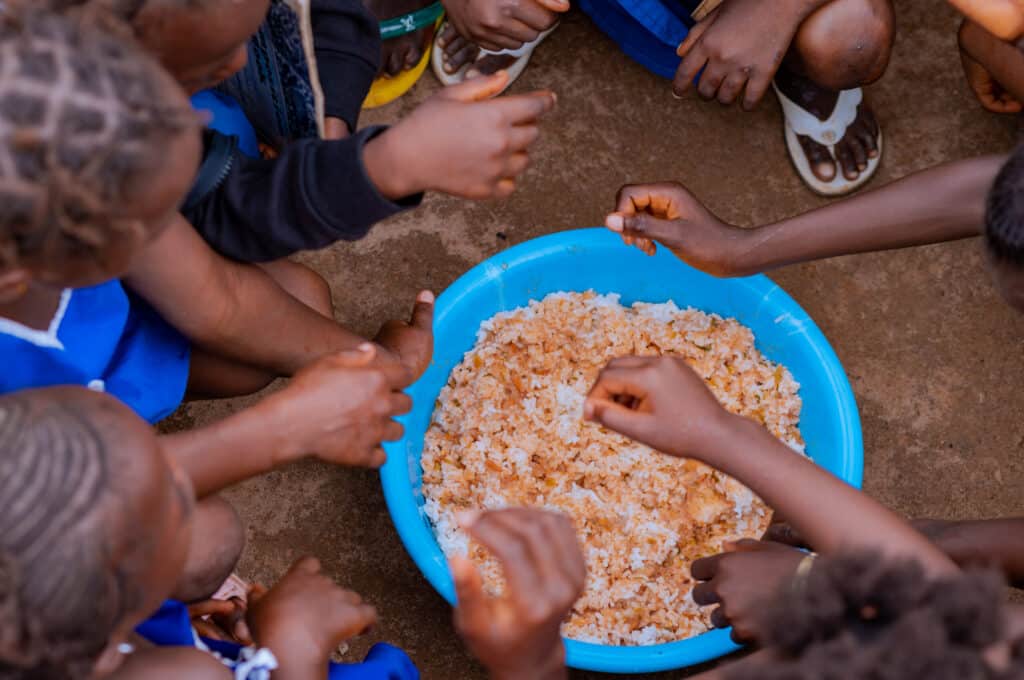 Children eating rice from blue basin together