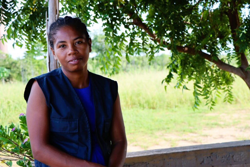 Woman outdoors near tree in vest.