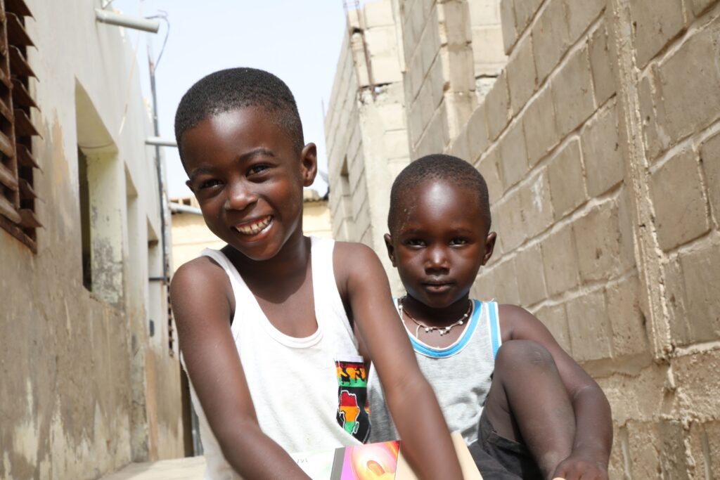 Boys sitting in alley holding books smiling