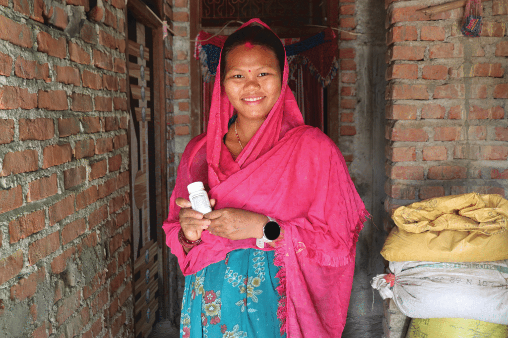 Woman in pink headscarf holding bottle of multiple micronutrient supplements for pregnant women