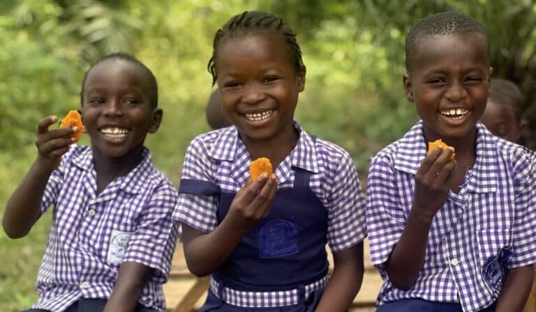 Three smiling children enjoy orange flesh sweet potatoes