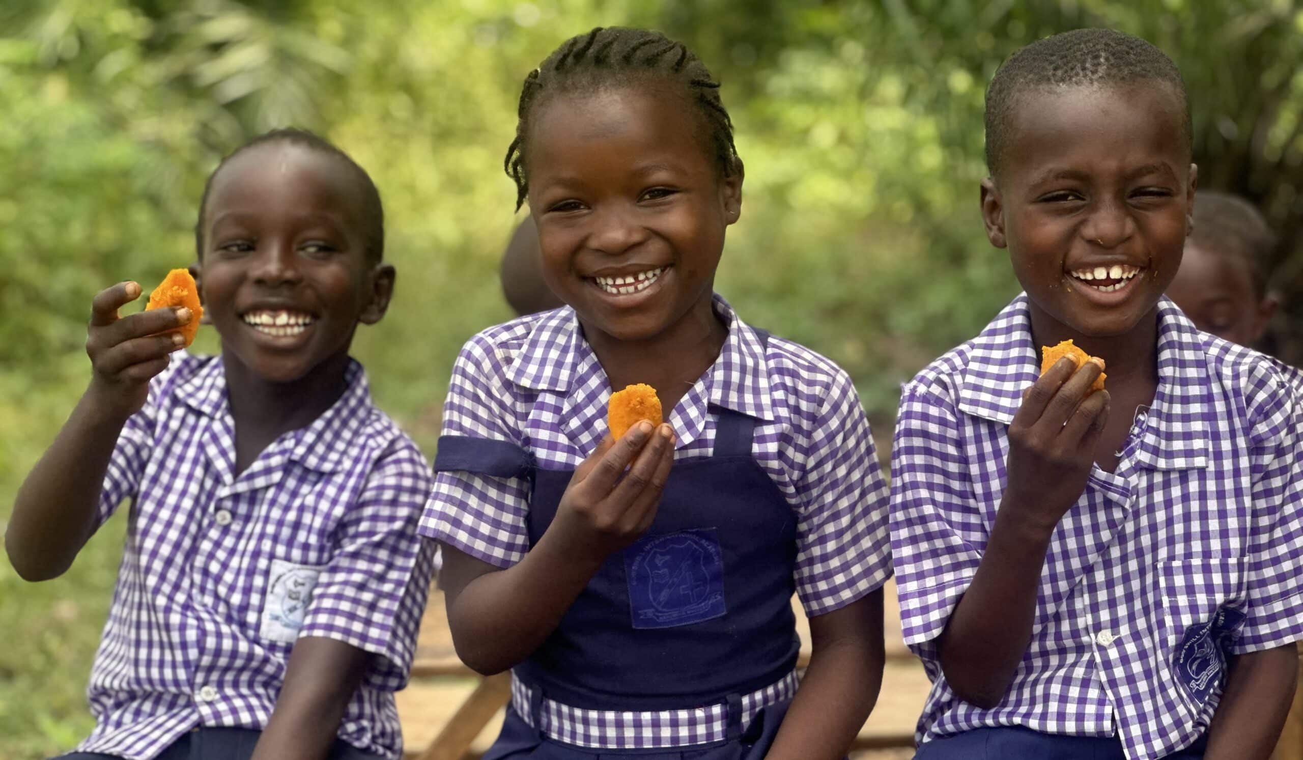 Three smiling children enjoy orange flesh sweet potatoes