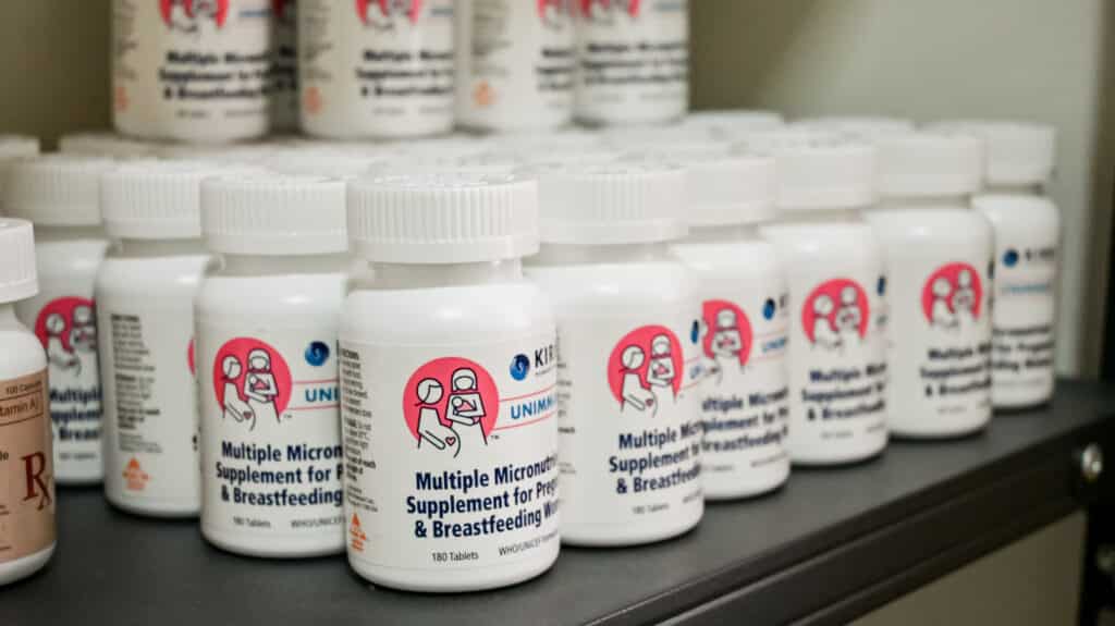 White bottles of Multiple Micronutrient Supplements for Pregnant and Breastfeeding Women arranged in rows on a shelf.